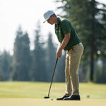 A person wearing a cap and green shirt is putting on a golf course.