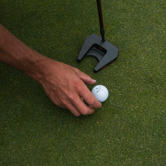 A person placing a golf ball next to a putter on a green.