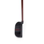A golf putter with a dark head and a red shaft is positioned on a white background.