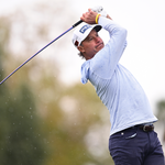 A person in a light blue shirt and white cap is swinging a golf club.